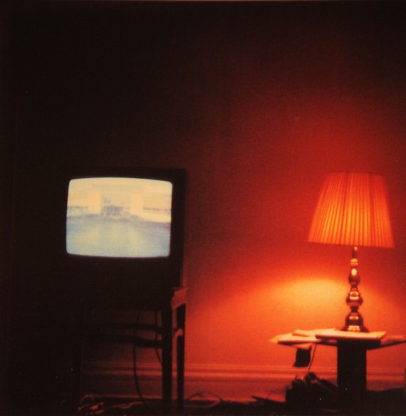 Polaroidbild, Ansicht eines Innenraums mit kleinem Fernseher und Tischlampe, rötliches Licht