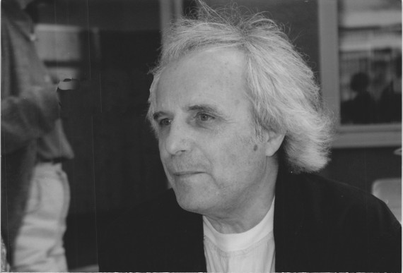 Schwarz-weiß-Porträt vom Künstler Johannes Haimerl. Dieser schaut nach links und ist bis zur Brust zu sehen. Er hat gräuliches Haar bis über die Ohren, trägt ein weißes T-shirt und eine schwarze Jacke darüber.