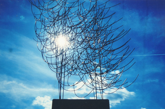 Metallkunstwerk von Johannes Haimerl aus vielen halbrund gebogenen Metallstäben vor wolkenlosem blauem Himmel, im starken Gegenlicht.