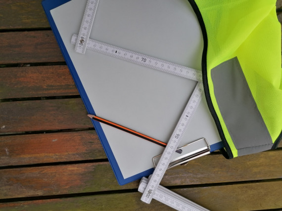 Meterstab, Bleistift Klemmbrett mit Papier und Sicherheitsweste auf einem Holztisch.