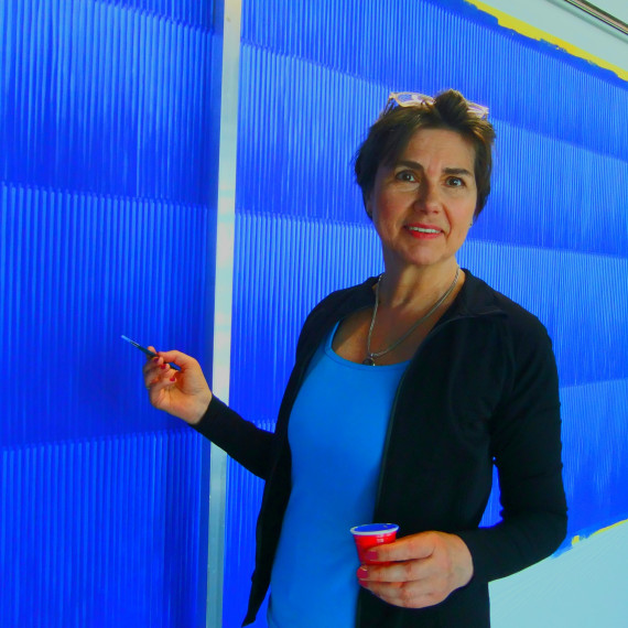 Künstlerin Astrid Schröder an einer Leinwand in dunkelblauer Farbe stehend und malend, den Blick zum Betrachter.