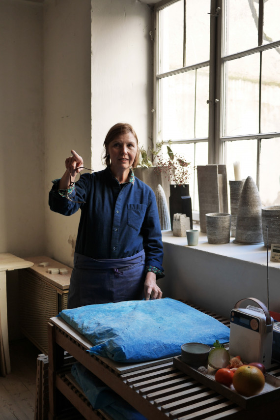Künstlerin Christine Wagner in ihrem Atelier an einem Tisch stehend und auf etwas außerhalb des Bildraums zeigend.