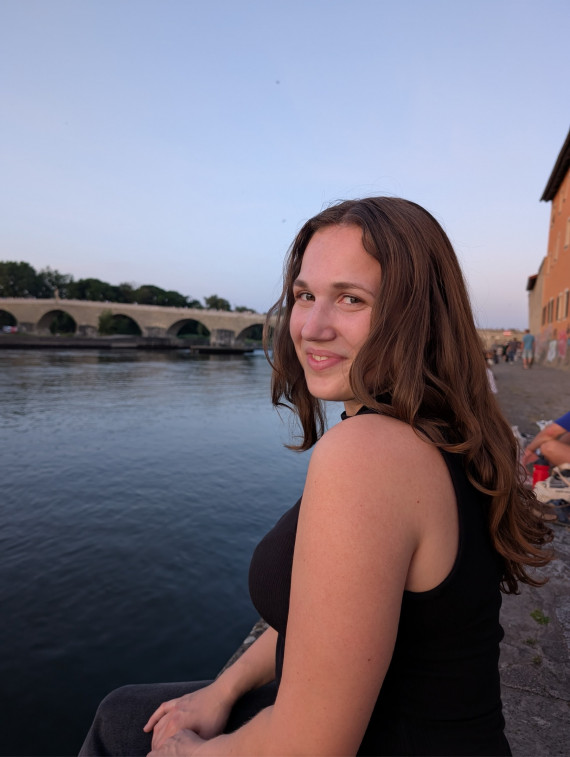 Junge Frau an einem See sitzend und lachend &uuml;ber die linke Schulter blickend.