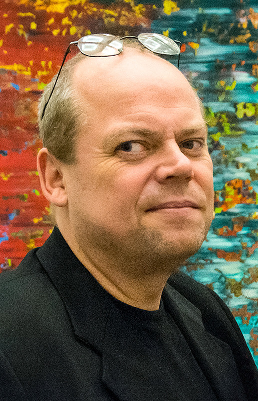 Portr&auml;t eines Mannes mit auf die Stirn geschobener Brille vor buntem Hintergrund