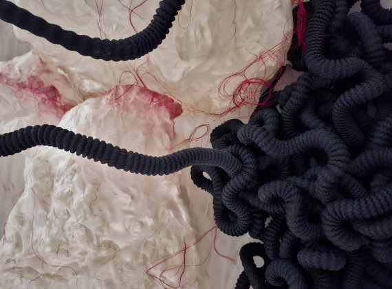 Detailansicht von einem mit roden F&auml;den durchzogenen Gewebe und schwarzen, geriffelten Schl&auml;uchen als Teil eines Kunstobjekts.