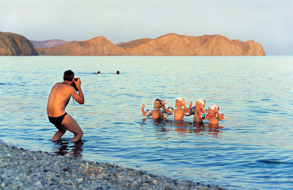 Foto eines Mannes in Badehose, der vier kleine jungen im Meer stehend fotografiert.